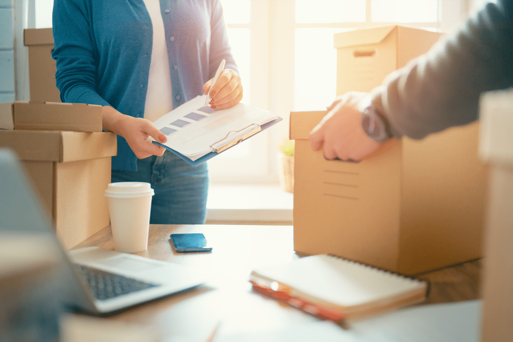 Woman holding a clipboard and man lifting a box from a table with business papers at AAA Self Storage in Chatsworth, California