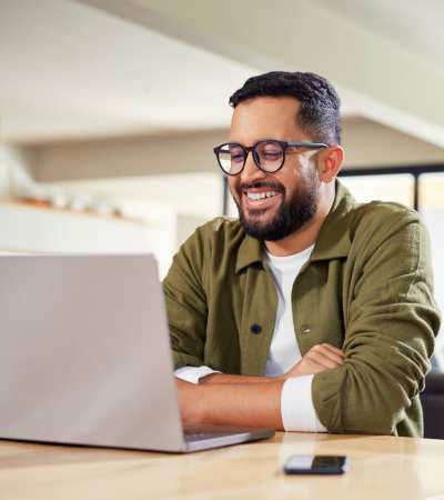 Man smiling while working on a laptop at a wooden table at Dutch Village Apartments in Baltimore, Maryland 
