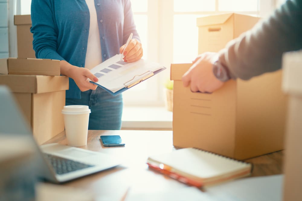 Woman holding a clipboard and man lifting a box from a table with business papers at A-American Self Storage in Hemet, California