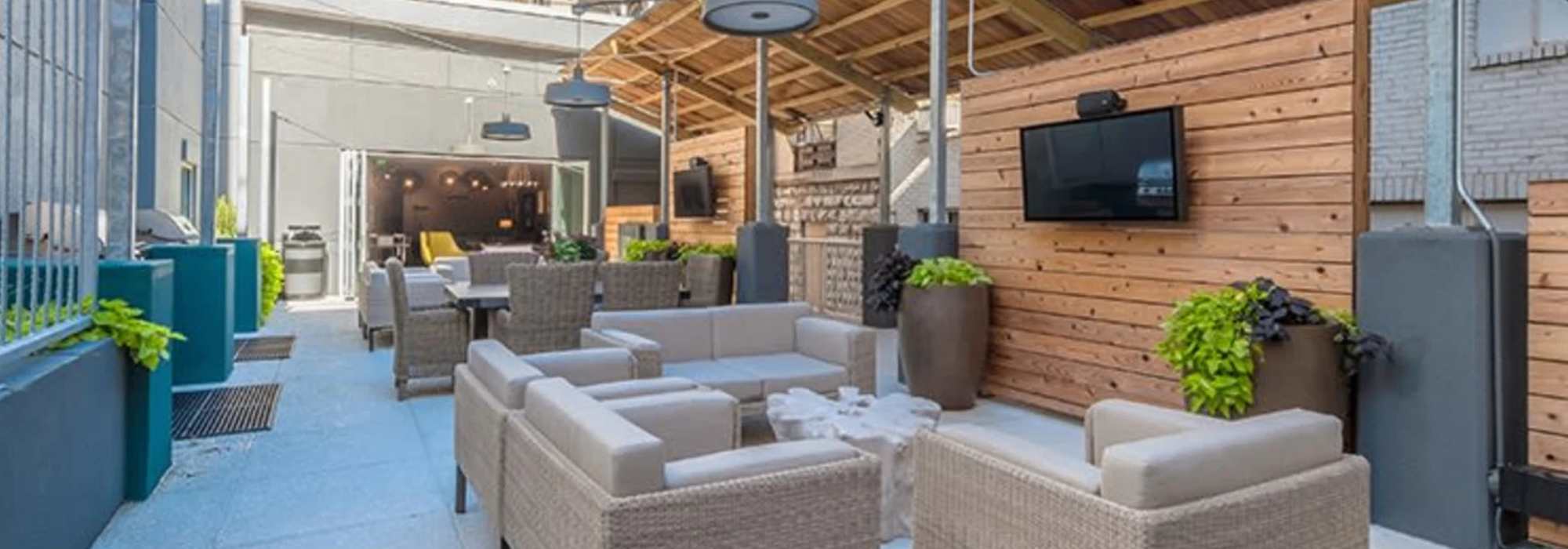 Downtown Nashville, TN, Apartments Near The Gulch Nashville - Cumberland on Church - Outdoor Lounge With Wicker Seating, Wood Accent Wall, Covered Patio, and Wall-Mounted Televisions.