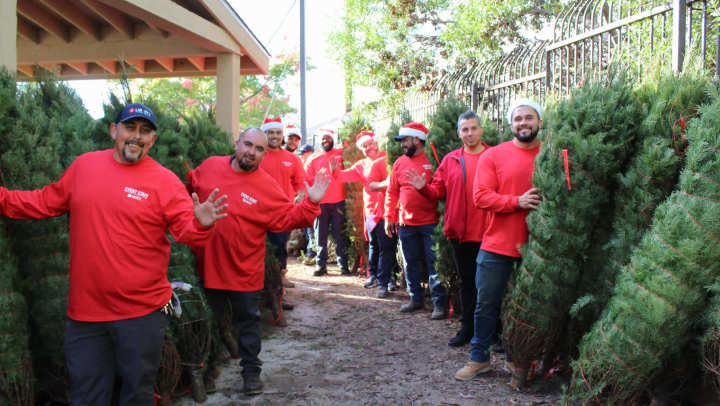 Liberty Military Housing employees in a line holding up Christmas Trees while smiling and waving at the camera. 