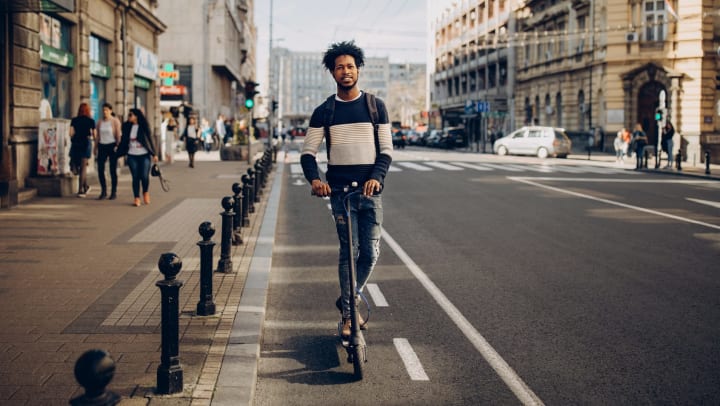 Man riding down the street on an electric scooter with a smile on his face. 