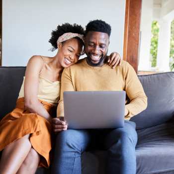 Couple enjoying time together on a couch, looking at a laptop, smiling and relaxed at Riverbirch in Ames, Iowa