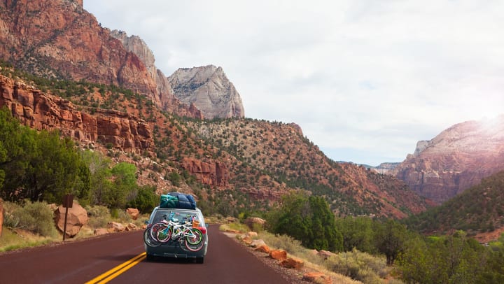 Car driving on the road in Utah with bicycles and camping gear strapped to the vehicle’s exterior.