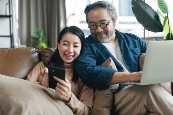 Couple on their phone and laptop on the couch in their apartment at Crockett Manor Senior in Crockett, Texas