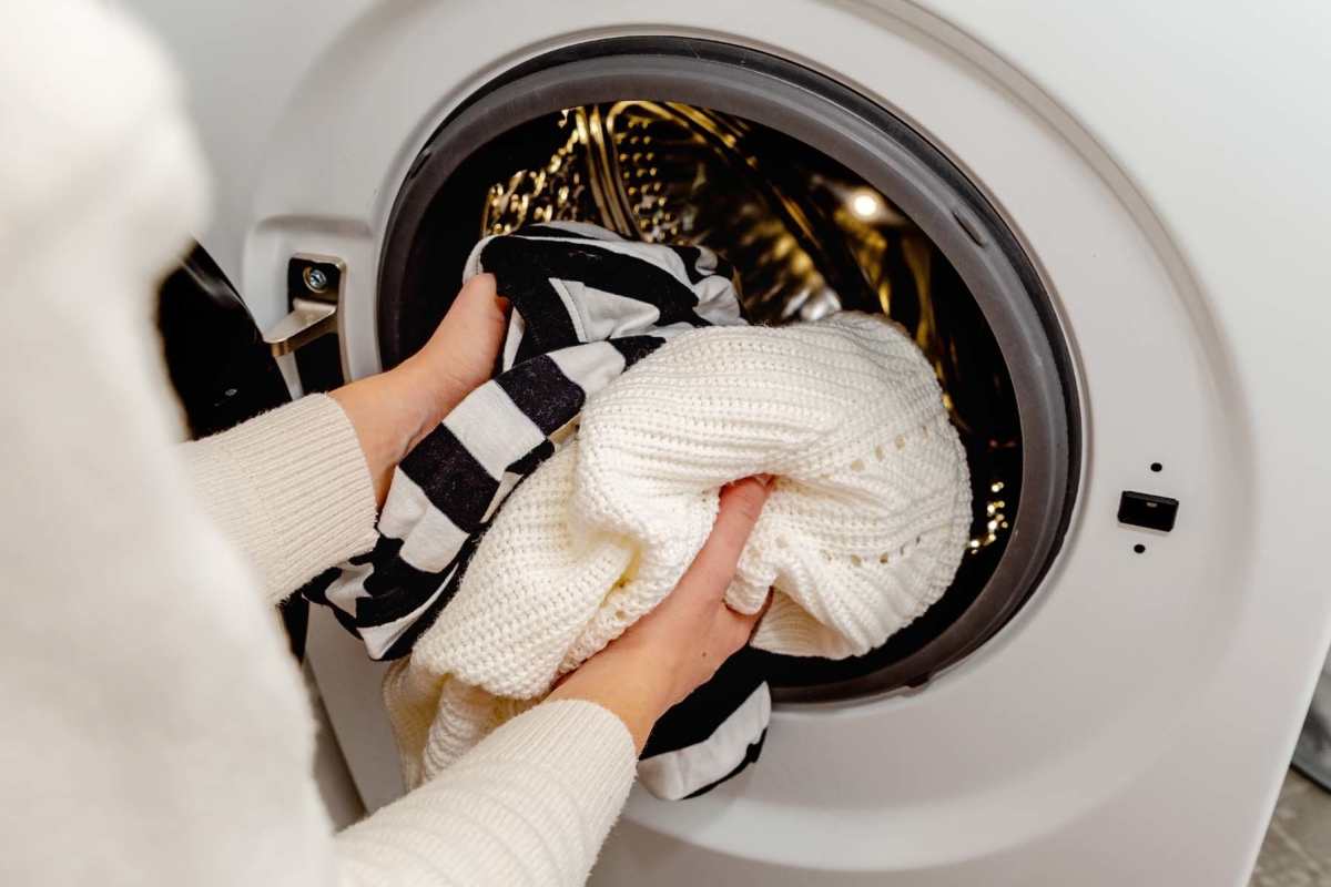Woman loading laundry into a front-loading washer holding a striped shirt and a white sweater at Seton Village Apartments in Emmitsburg, Maryland