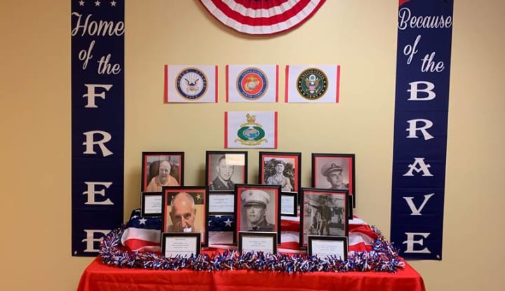 Table display of pictures of armed service members who live at Wesley Haven Villa, flanked by ribbons that say Home of the Free and Because of the Brave