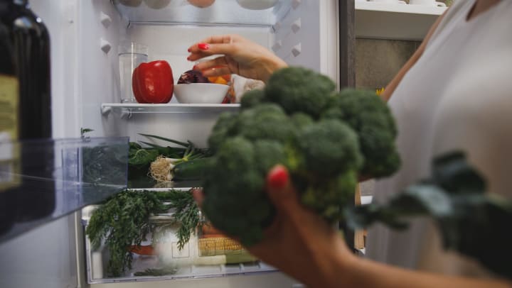 person holding broccoli while organizing the fridge | apartment prep before vacation