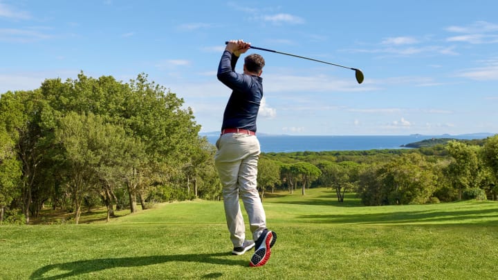 Golfer swings a golf club while overlooking the green. 