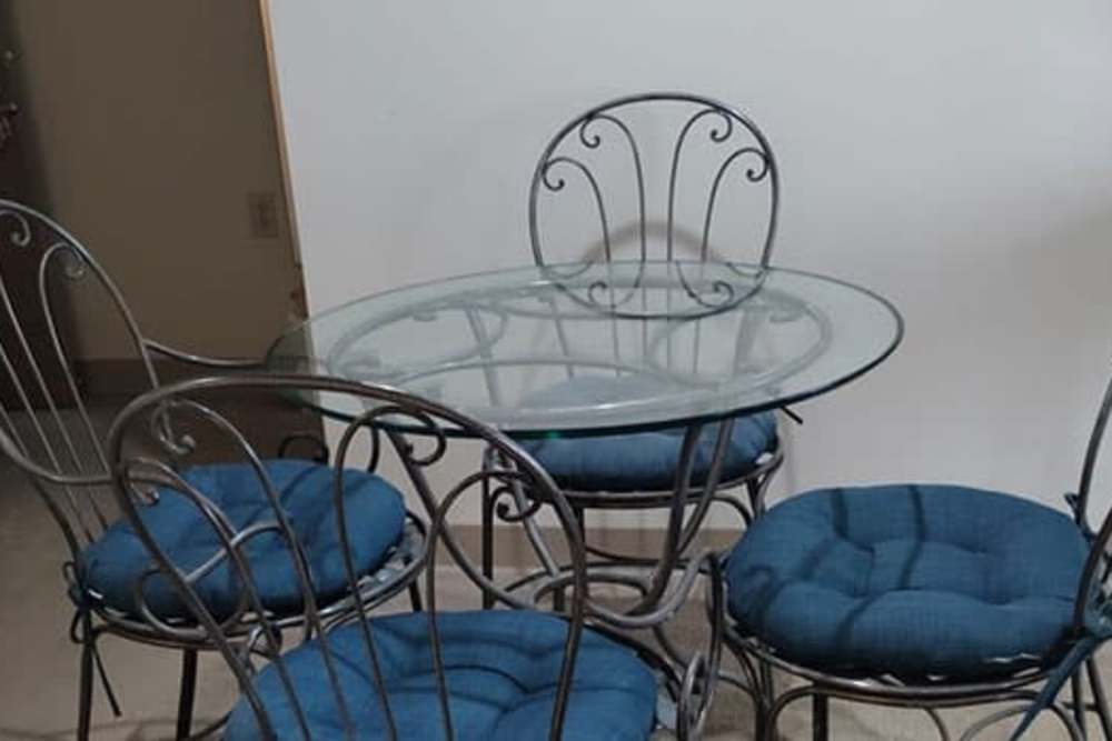Glass-top dining table with iron chairs and blue cushions in an apartment setting at Spencer Village in Eldersburg, Maryland