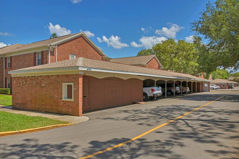 Brick apartment community carport area with covered parking spaces and storage units beside a residential building under a clear sky at Carlton Arms Of Winter Park in Winter Park, Florida
