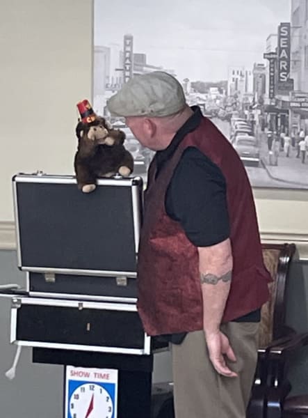 Magician talks to a monkey puppet perched on a medium-sized open case