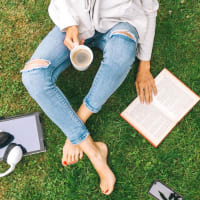 A woman sitting in the grass holding a cup of coffee and reading a book near Liberty Mill in Germantown, Maryland