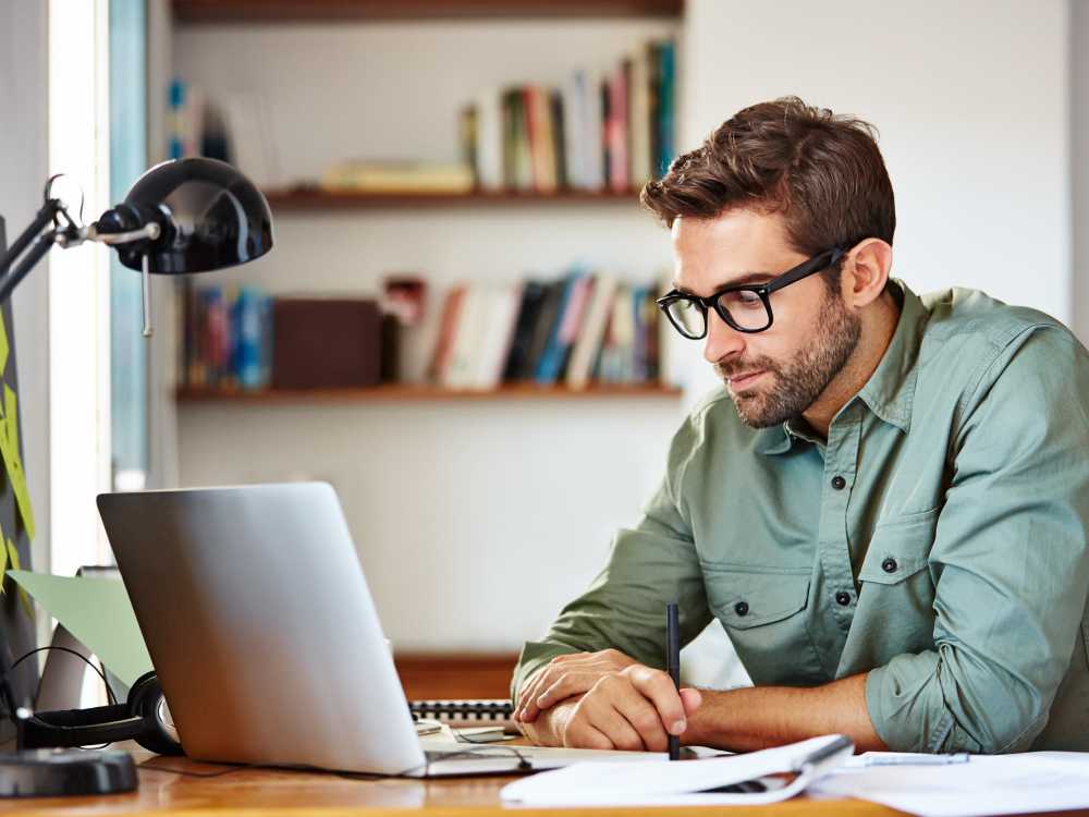Man working at desk with laptop and notepad in modern home office setting at South Oak in Ames, Iowa