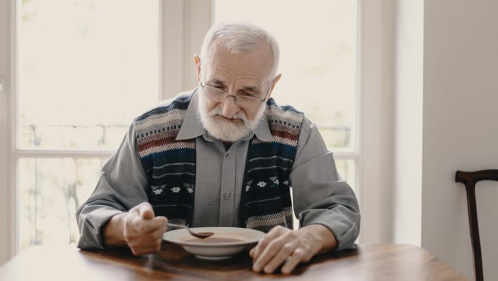 Sad lonely senior man eating soup in empty apartment.