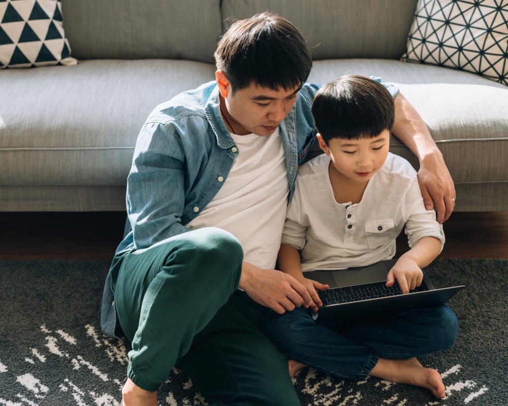 Dad and kid sitting on the floor looking at social media on the laptop at Sofi at Wood Ranch in Simi Valley, California