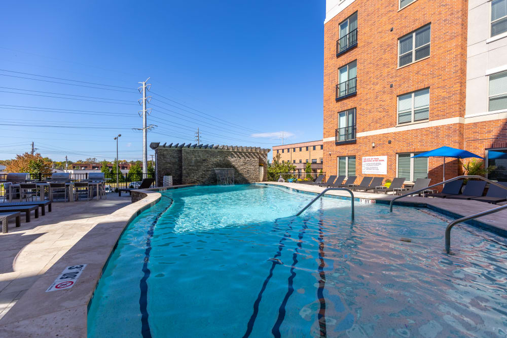 Dog-Friendly Apartments in Clayton, MO - The Barton - Pool with Grill Area, Tables with Chairs, Lounge Chairs, and Umbrellas