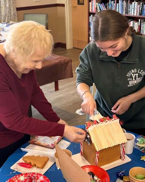 Resident and staff member building a gingerbread house