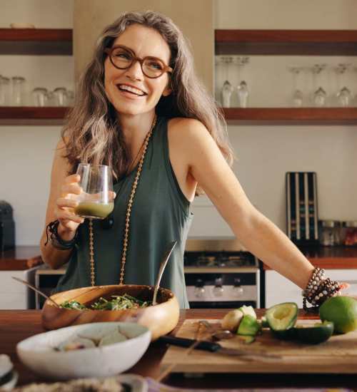 A woman with glasses smiles warmly while holding a glass of wine at EVOQ East Cobb in Marietta, Georgia