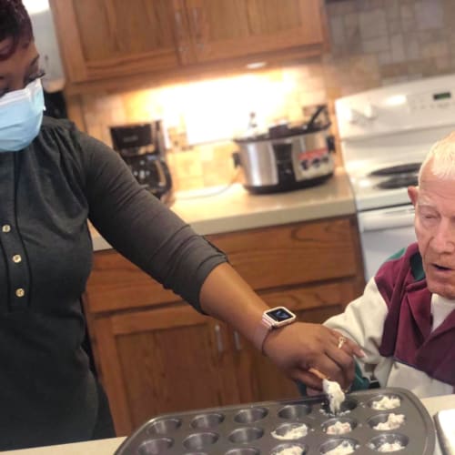 Masked caretaker cooking with a resident at Oxford Glen Memory Care at Sachse in Sachse, Texas