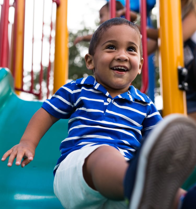 Resident child having fun on the slide at a playground in one of the many parks near Meadow Walk Apartments in Miami Lakes, Florida