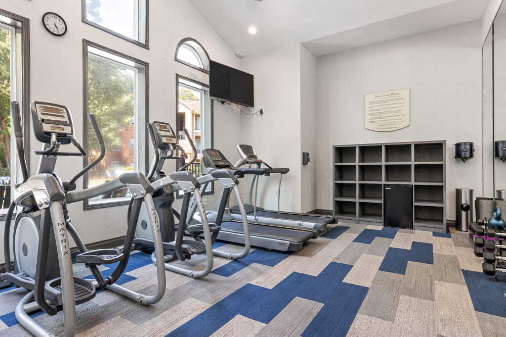 Treadmills and ellipticals machines in fitness room with large, wall-mounted tv monitor at Marquis at Kingwood in Kingwood, Texas