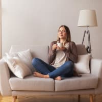 A woman sitting on a couch holding a cup of coffee at The Station at Brighton in Grovetown, Georgia