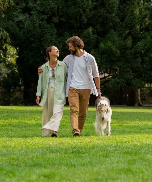 Couple walking together in a grassy park with a dog, enjoying a sunny day at Dutch Village Apartments in Baltimore, Maryland