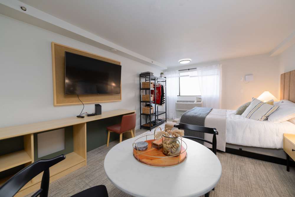 Furnished model apartment home with queen size bed with headboard, flat screen TV, and wardrobe organizer with desk at Thea Apartments in Tacoma, Washington.