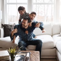 A man playing with his children on his back in their couch at Evergreens at Mahan in Tallahassee, Florida