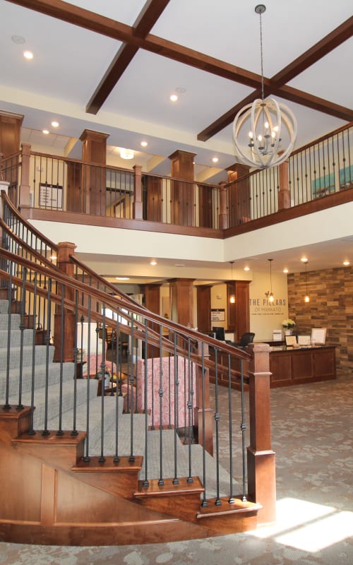 Beautiful lobby with hanging chandelier and curved wooden staircase at The Pillars of Mankato in Mankato, Minnesota