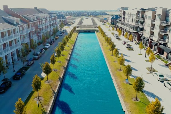 Walkway between apartment buildings with a serene water feature running through the center, creating a peaceful and scenic environment.