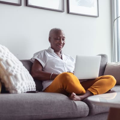 A woman using her laptop smiling on her couch at Mariposa at Clear Creek in Webster, Texas