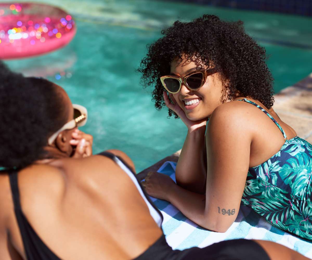 Two women in swimsuits relax by a pool at Caprock Crossing in College Station, Texas