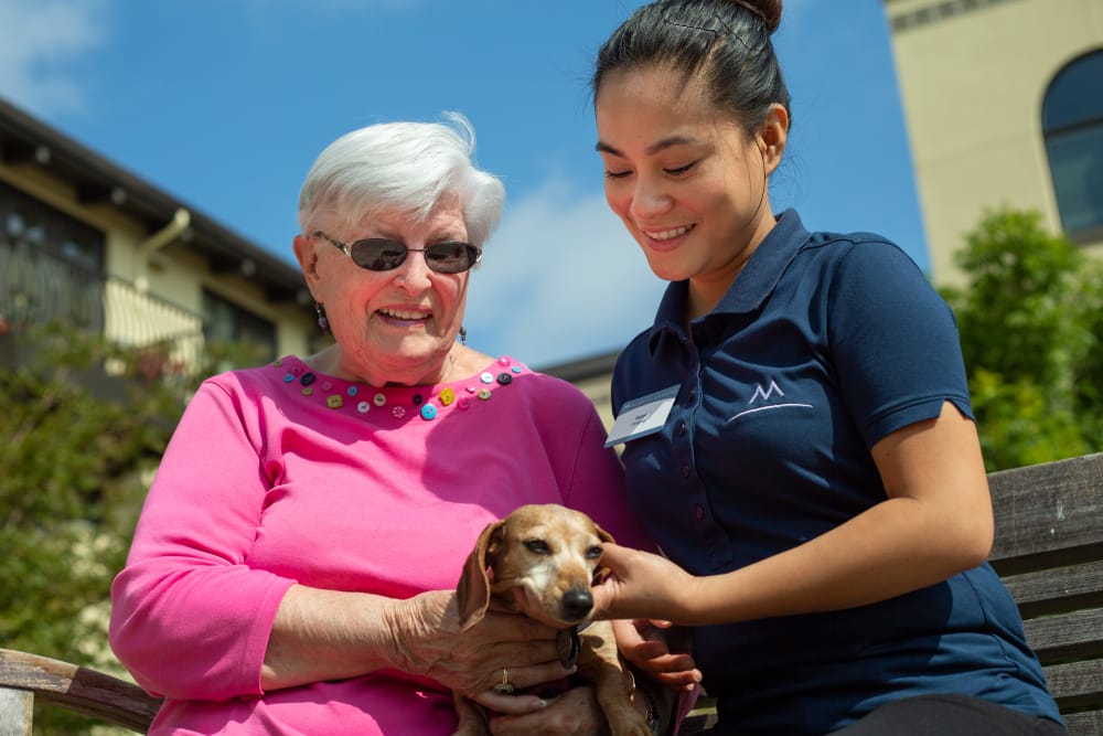 Resident smiling with a pet and caregiver at Merrill Gardens at Campbell in Campbell, California. 