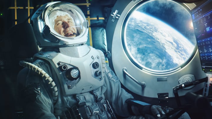 A male astronaut inside a space capsule in space. Planet earth can be seen from the window.