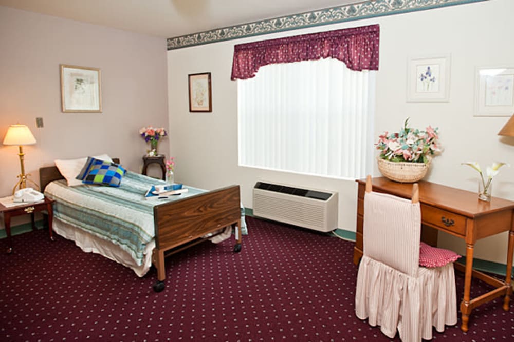 Serene senior living apartment with bed, table, and red carpeting at Cambridge Square Assisted Living in Rosenberg, Texas