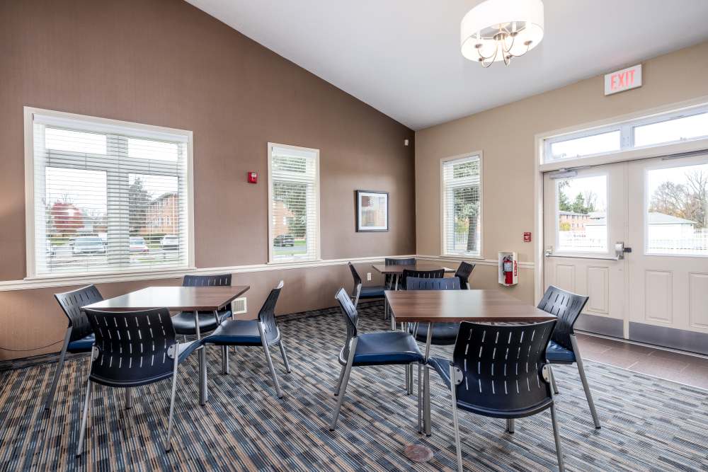 A bright lit common area with several tables and chairs at Greece Commons Apartments in Rochester, New York
