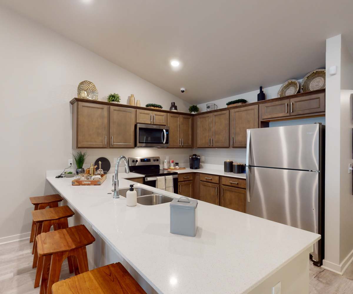 Modern kitchen with stainless-steel appliances, island counter with quartz countertop and barstool at Insignia Apartments in Clarkston, Michigan