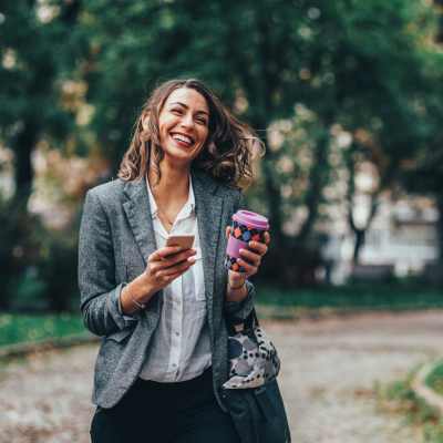 Women walking in a park with her phone and a cup of coffee at Westmont Village in Charlotte, North Carolina