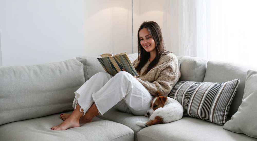 A resident reading a book in her living room with a pet dog by her side at The Millwright in Cornelius, North Carolina