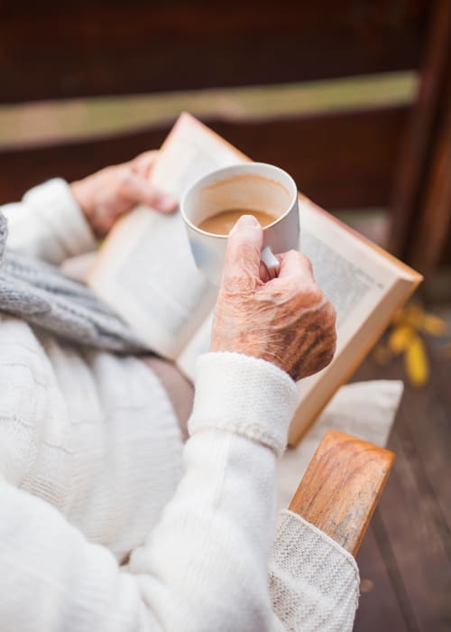 A close-up view of a old lady's hand holding a cup of coffee over a book at The Pillars of Prospect Park in Minneapolis, Minnesota