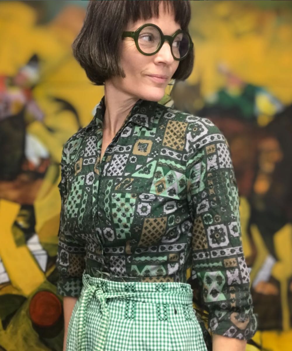 Rachael Van Dyke wearing green patterned shirt with bold, dark framed eyeglasses.