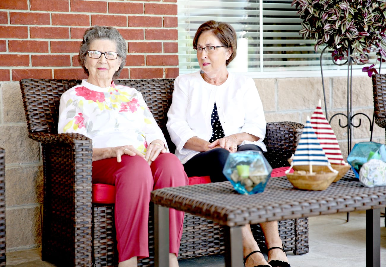 Two women sitting on an outside patio in outdoor furniture at Providence Assisted Living in Clarksville, Arkansas