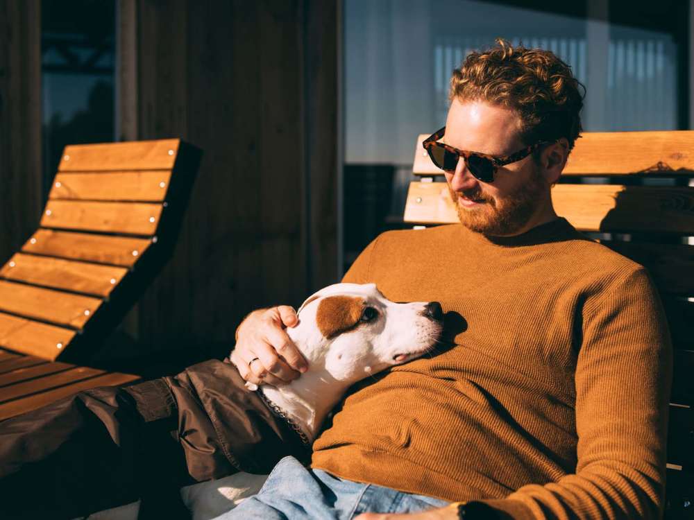 Resident relaxing on a wooden lounge chair with a dog in his lap, both enjoying the sun at 43 North Apartments in Grand Haven, Michigan