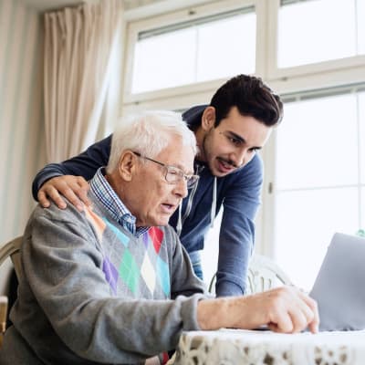 Assisted living resident getting some help with his laptop from a caregiver at 6th Ave Senior Living in Tacoma, Washington