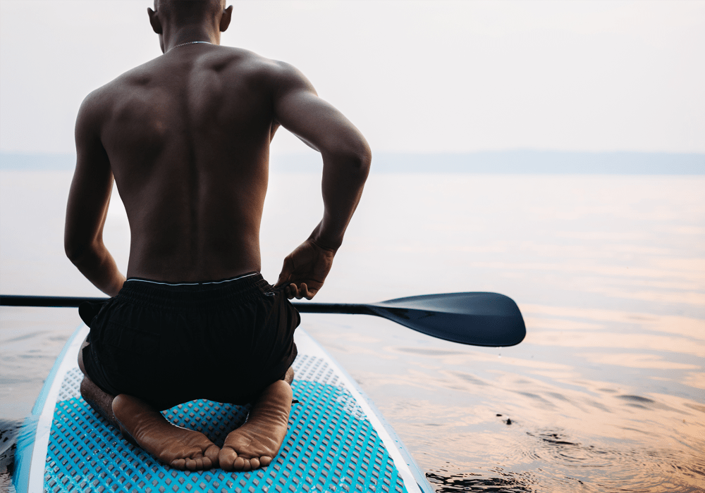 Man on a standup paddle board sitting on his knees at BB Living Light Farms in Celina, Texas