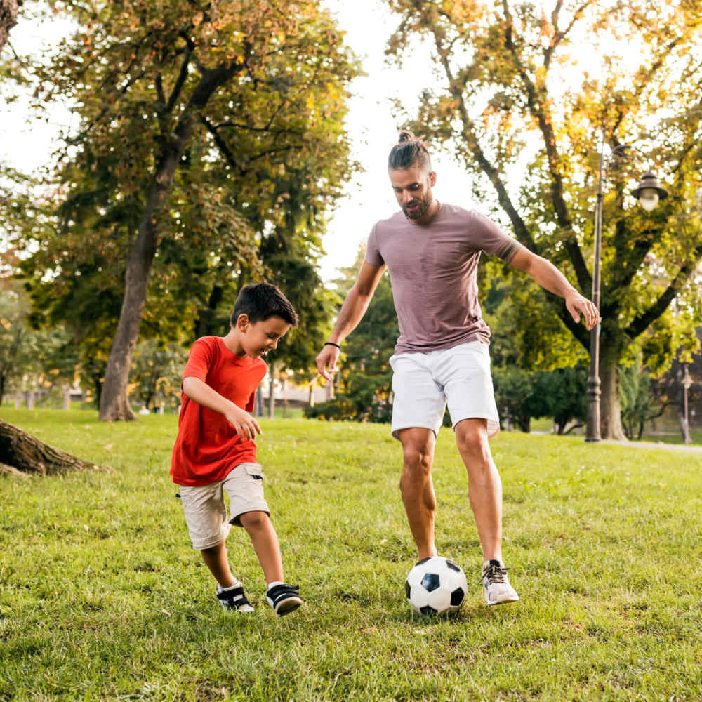 Resident playing soccer with his son at a lush green park near Pine Tree Apartments in Winston, Oregon