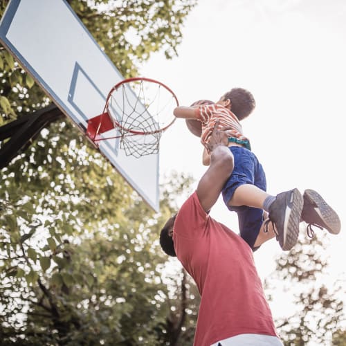 A father holding his son playing basketball at The Village at NTC in San Diego, California