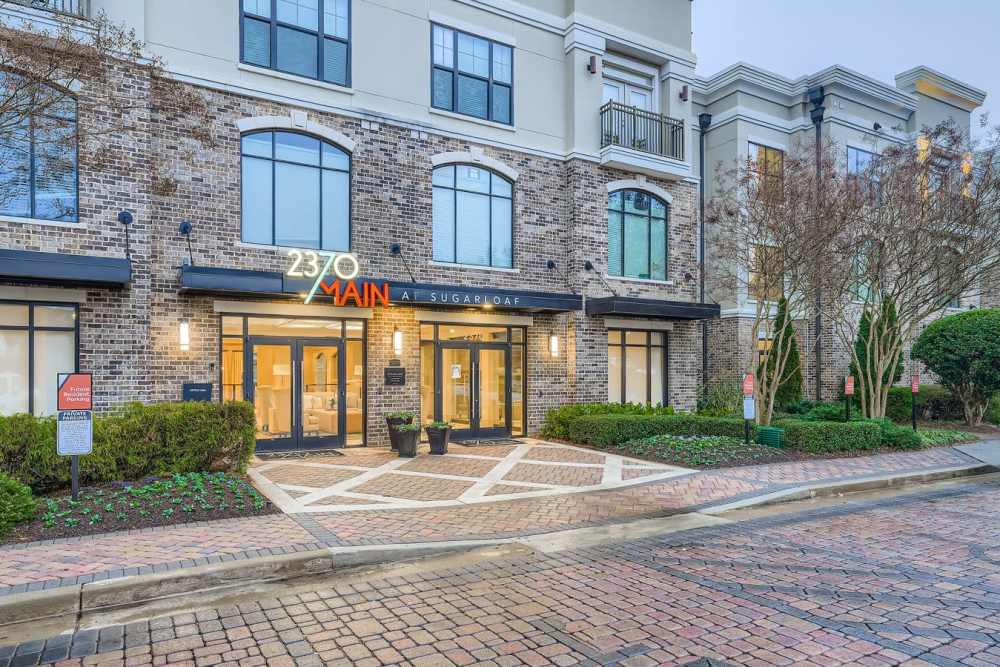 Charming entrance to 2370 Main at Sugarloaf, featuring elegant brickwork, vibrant landscaping, and inviting glass doors that welcome you home at 2370 Main at Sugarloaf in Duluth, Georgia